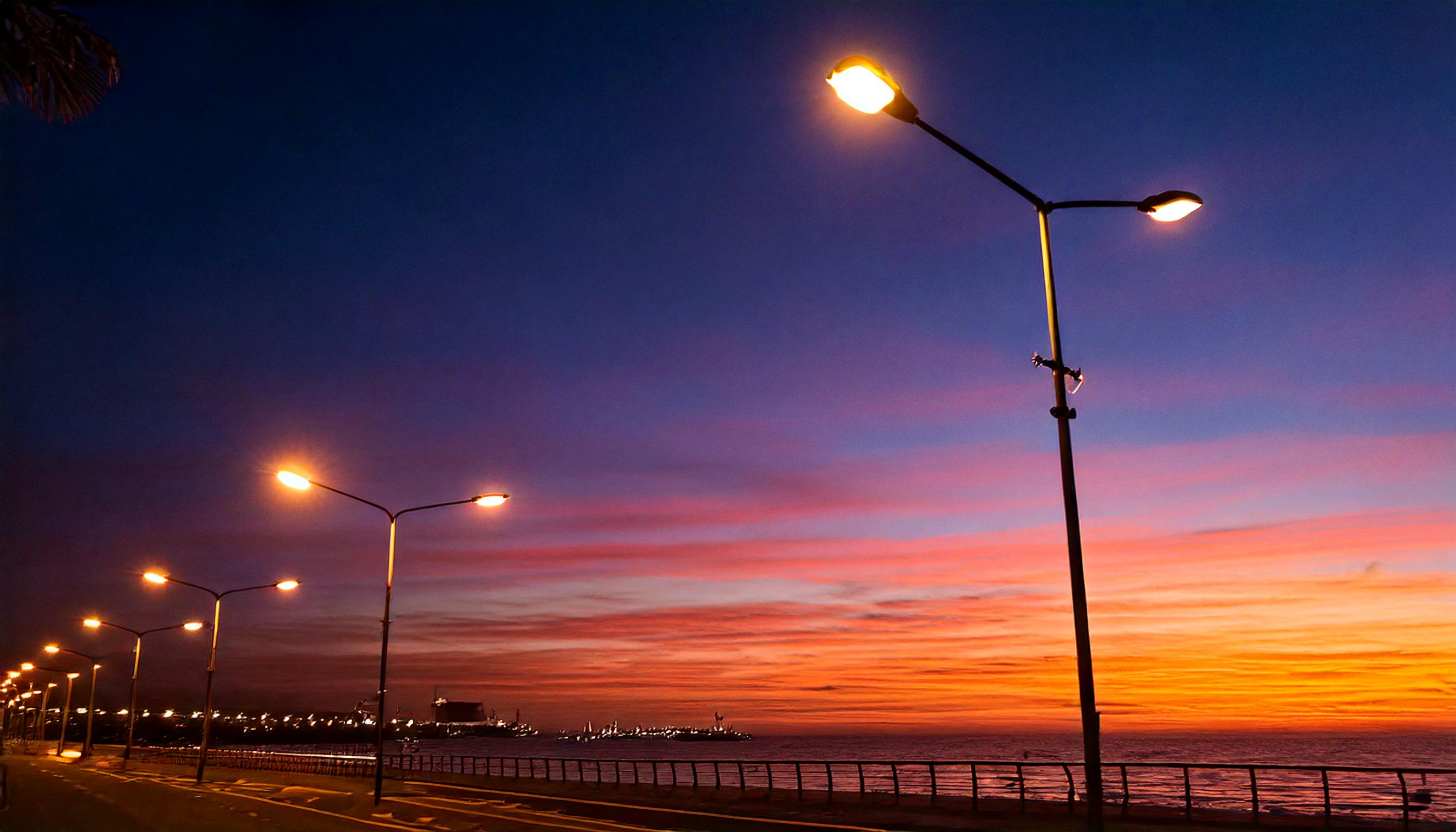 AuDHD special interest - Streetlights glowing at dusk along a seafront, with a vivid orange and purple sunset in the background
